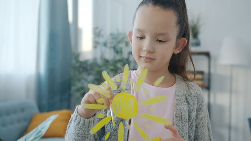 Devojčica crta sunce markerom na staklu, učestvujući u kreativnoj igri