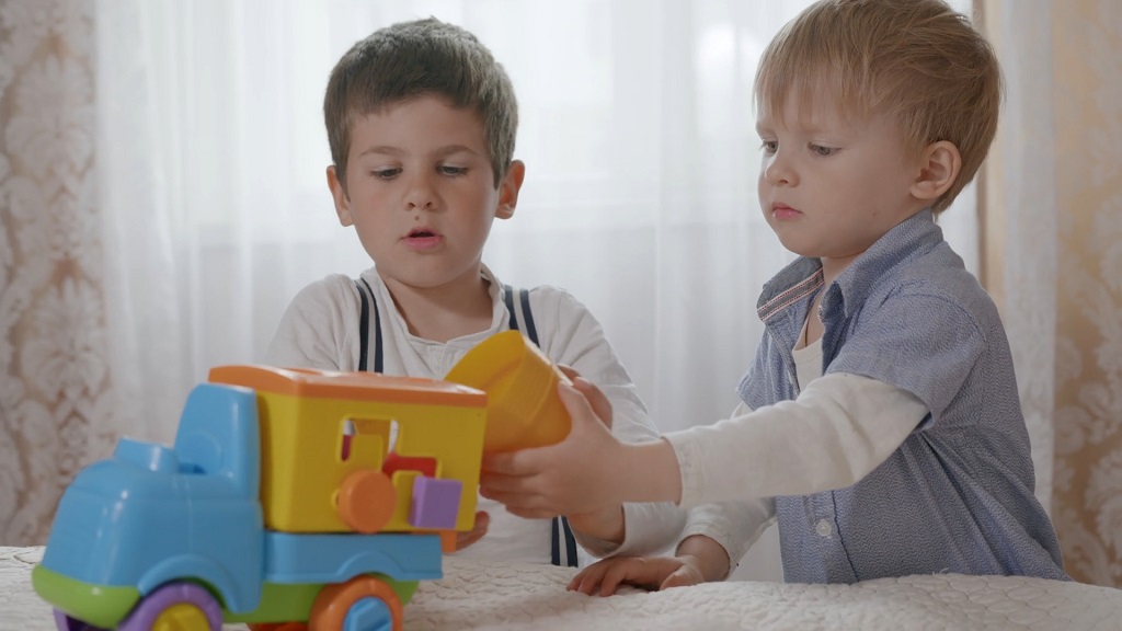 Dva dečaka sarađuju dok se igraju plastičnim kamionom