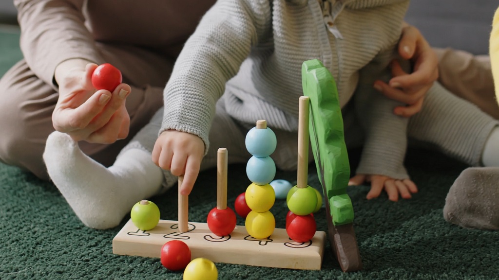 Mališan se igra edukativnom igračkom uz podršku odrasle osobe, u Montessori okruženju